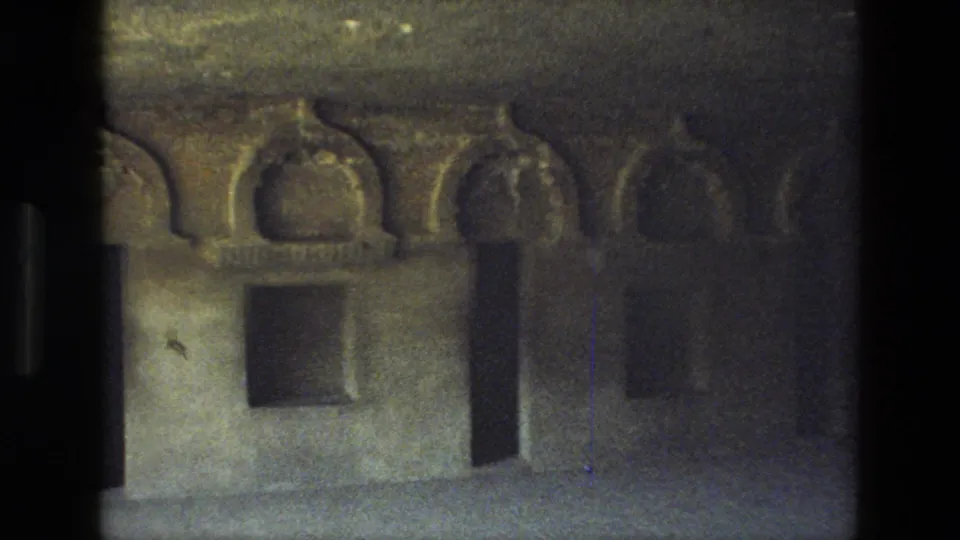 1974 visitor-shot 8mm frame showing carved cave-temple arches, a dark doorway, and worn stone surfaces in India.