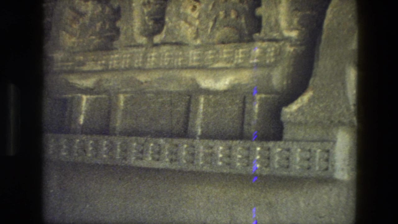 Close view of weathered carved stone architecture with dark film-edge shadows.