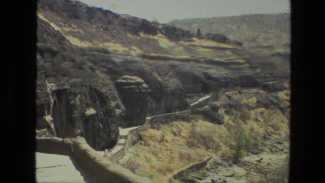 Rock-cut cave openings and a stone path on a dry canyon slope.