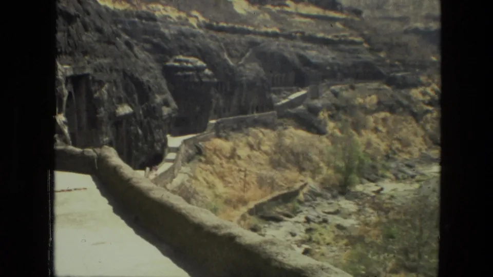 Visitor-shot 1974 India footage frames a stone walkway, steps and cave openings cut into rugged canyon rock.