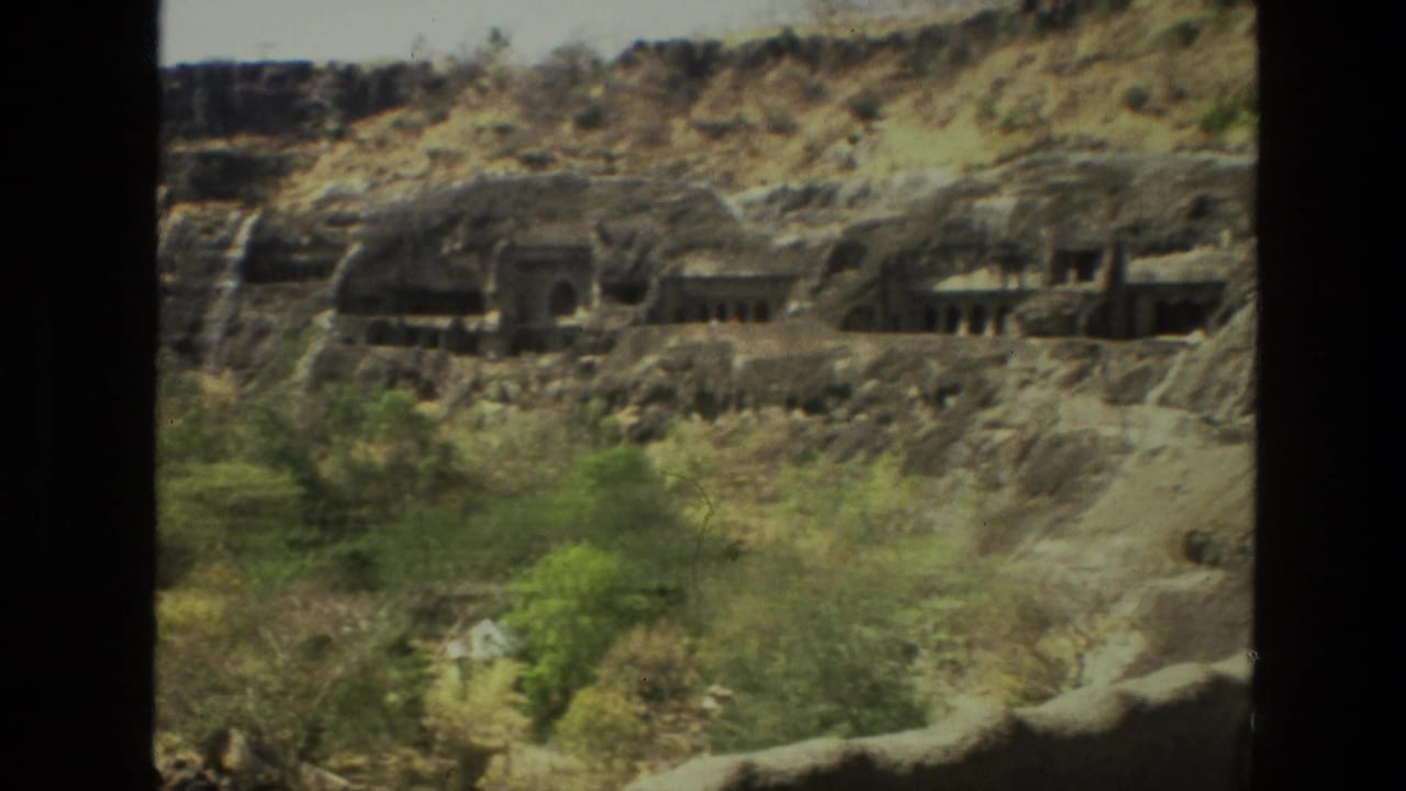 Panoramic cliffside view with cave entrances and trees below.