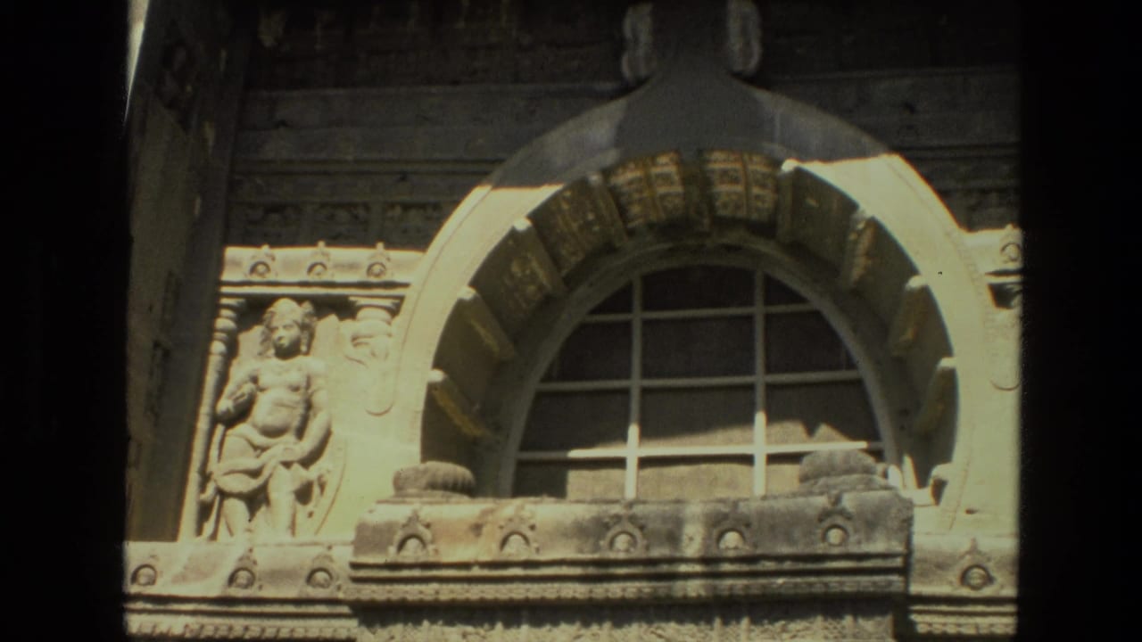 Ornate stone facade with an arched gridded window and carved figure beside it.