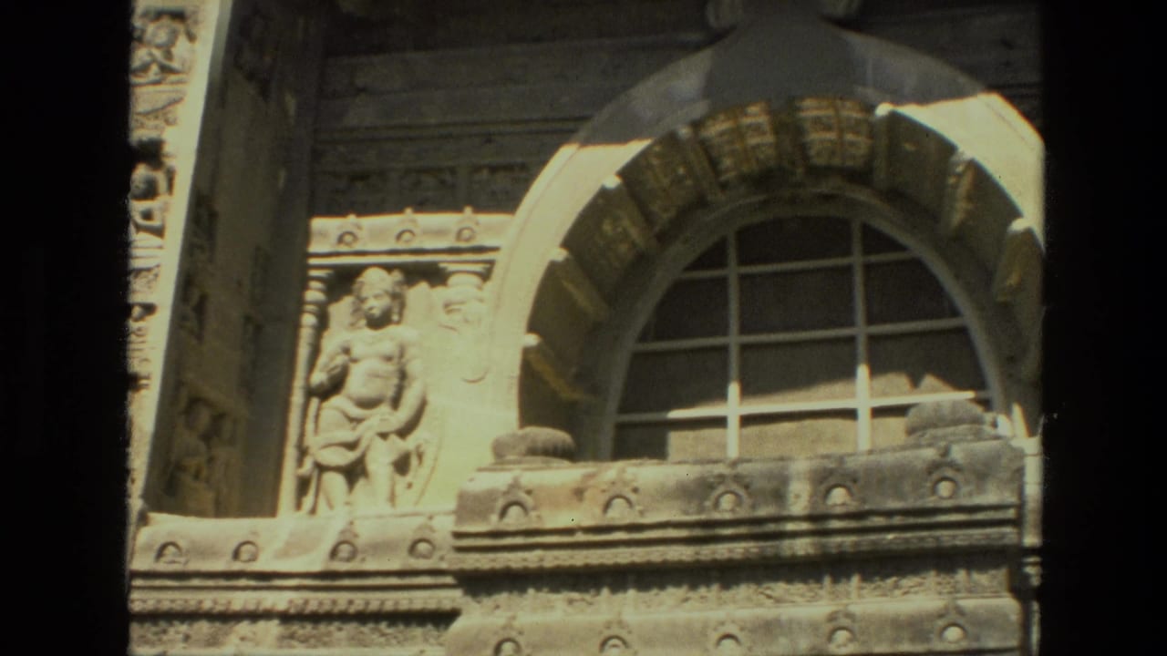 1974 India 8mm view of a temple facade detail, with a gridded arched window, carved stone bands, and a figure sculpture.