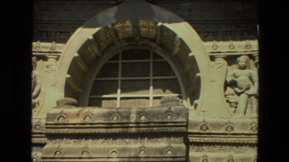 1974 India home-movie frame focused on an ornate temple wall with an arched window, carved ledges, and a sculpted figure.