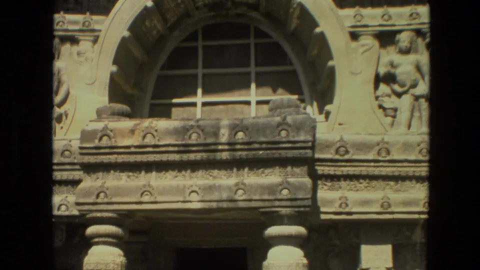 1974 India 8mm frame showing a temple facade section with an arched gridded window, stone figure, and partial lower column.