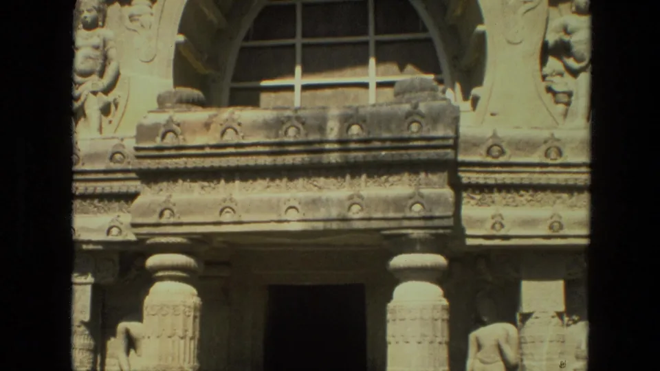 1974 India 8mm frame showing an ornate carved stone facade with an arched opening, sculptural panels, columns, and a shadowed entrance.