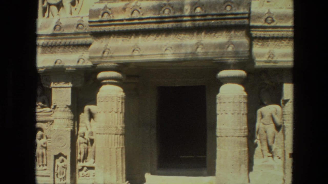 Closer view of carved stone columns, sculpted figures, relief panels, and a dark entrance.