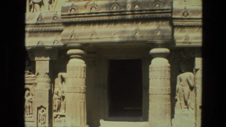 1974 India travel frame focused on a stone entrance with carved columns, sculpted human-like figures, and decorative relief work.