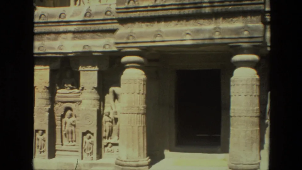 1974 India frame of a carved stone building entrance, with heavy columns, human-like sculptural reliefs, and a dark recessed doorway.