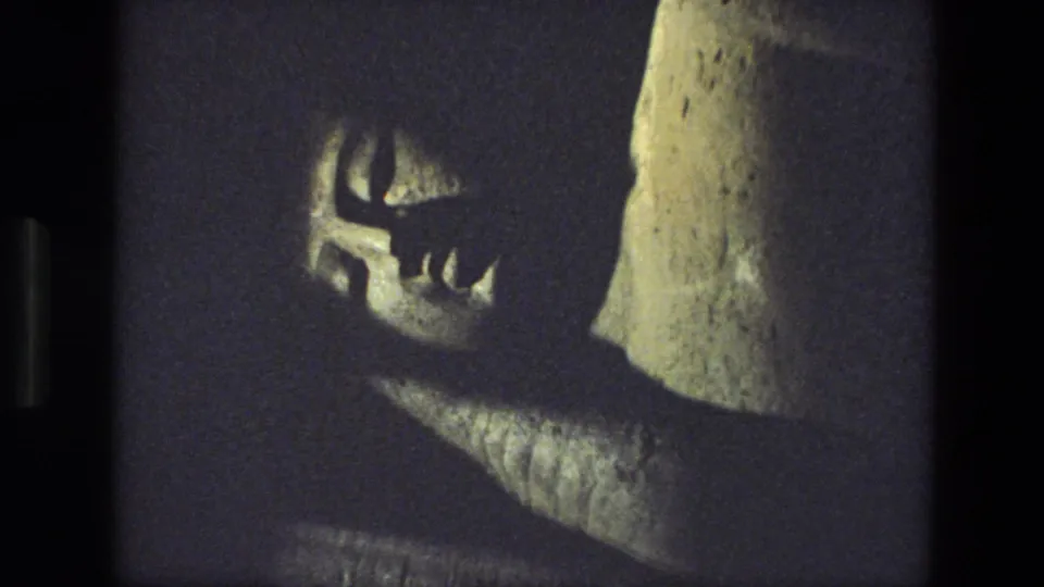 1974 India 8mm frame with a low-lit view of a large reclining stone figure, including its face, arm-like form, and pedestal area.