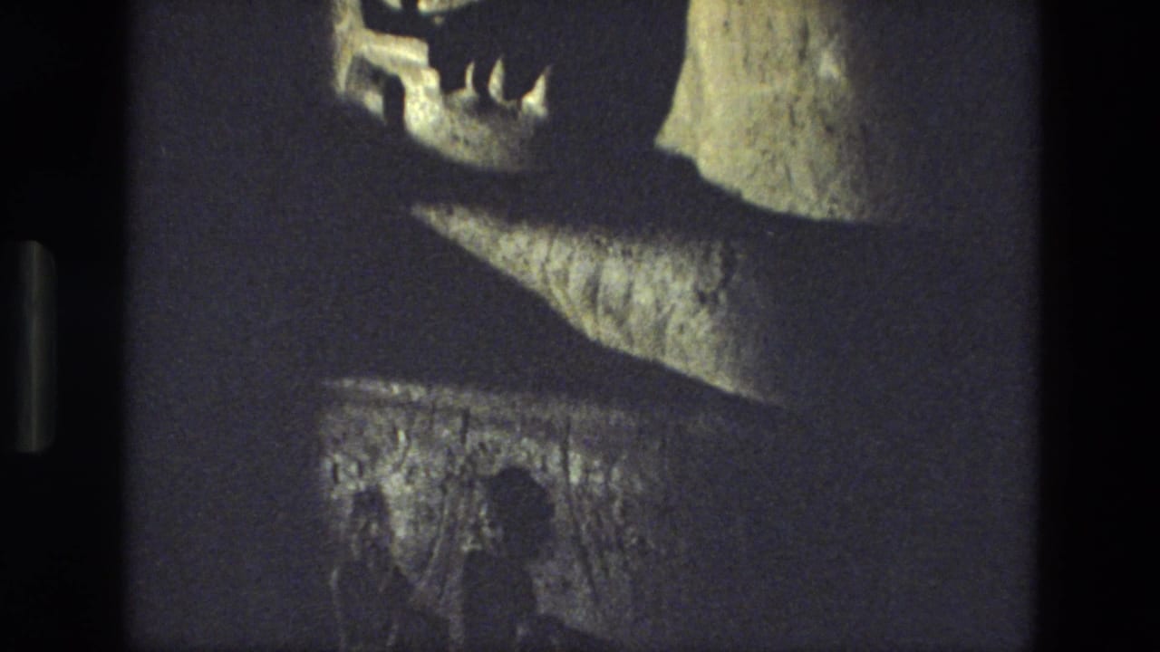 1974 India travel footage frame showing the face and upper portion of a reclining stone statue under dim lighting.