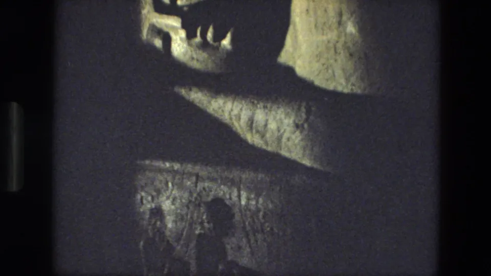 1974 India travel footage frame showing the face and upper portion of a reclining stone statue under dim lighting.