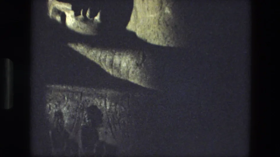 A grainy 1974 India 8mm frame shows the reclining statue from a slightly shifted angle, emphasizing the face, ledge, and base.