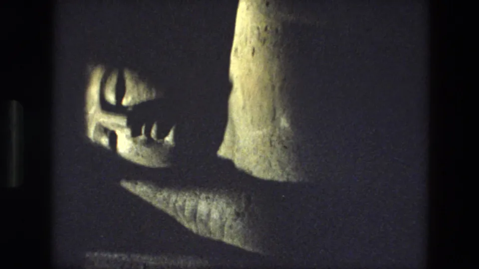 Final 1974 India frame with the reclining stone figure partly obscured by darkness and a tall stone surface at right.