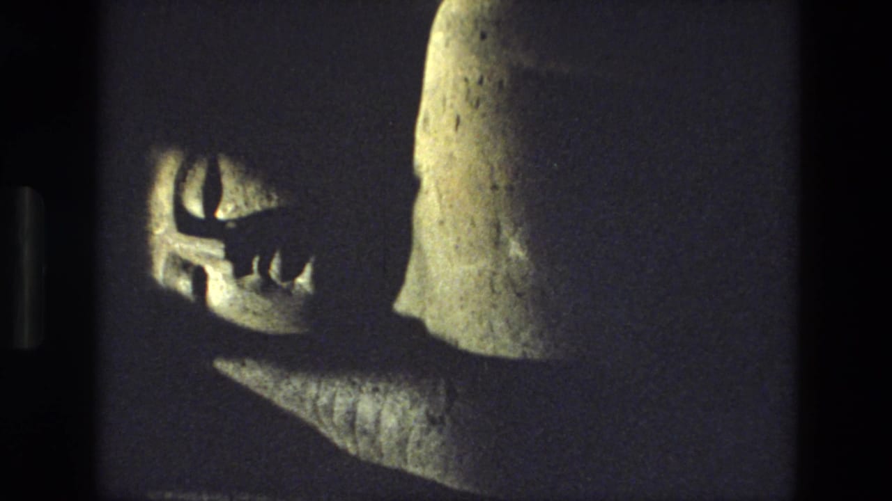 1974 8mm India travel frame showing a close, shadowed view of a carved stone figure or sculpture detail inside or near a rock-cut site.