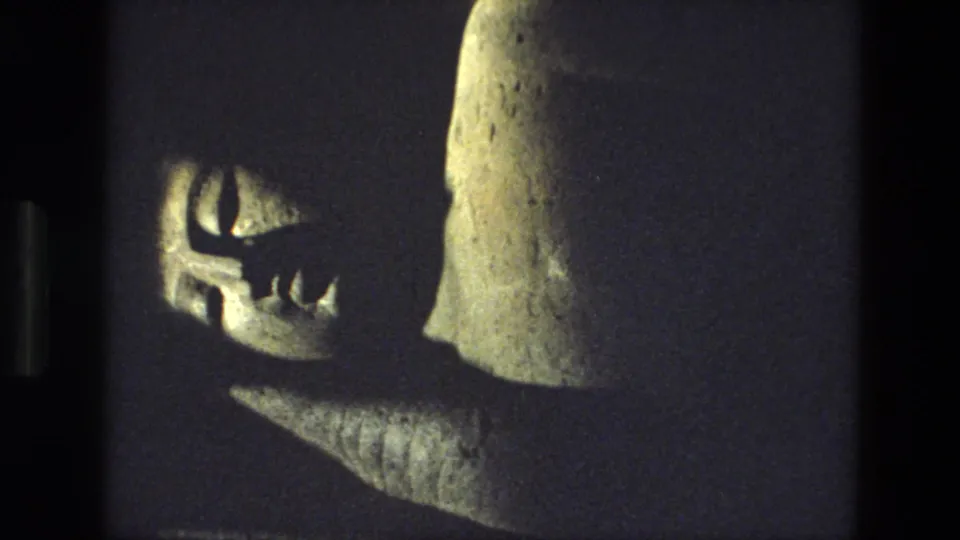 1974 8mm India travel frame showing a close, shadowed view of a carved stone figure or sculpture detail inside or near a rock-cut site.