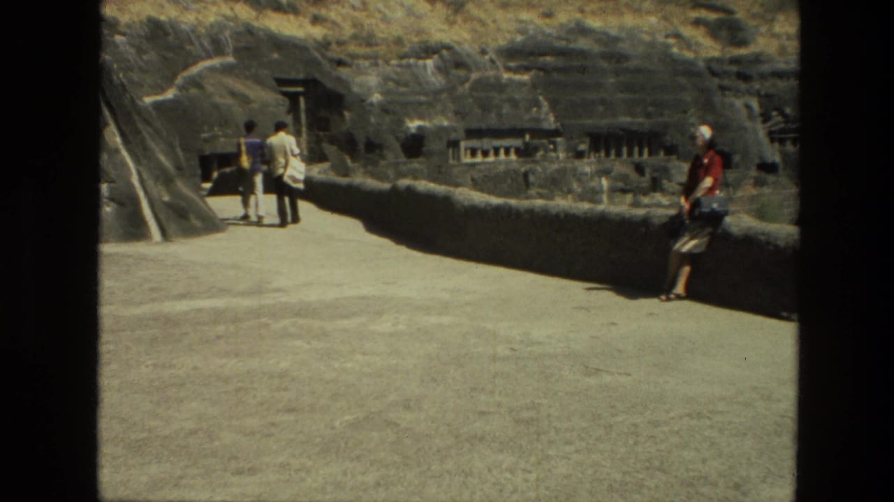 Tourists walk along a paved path beside carved rock walls and cave openings.