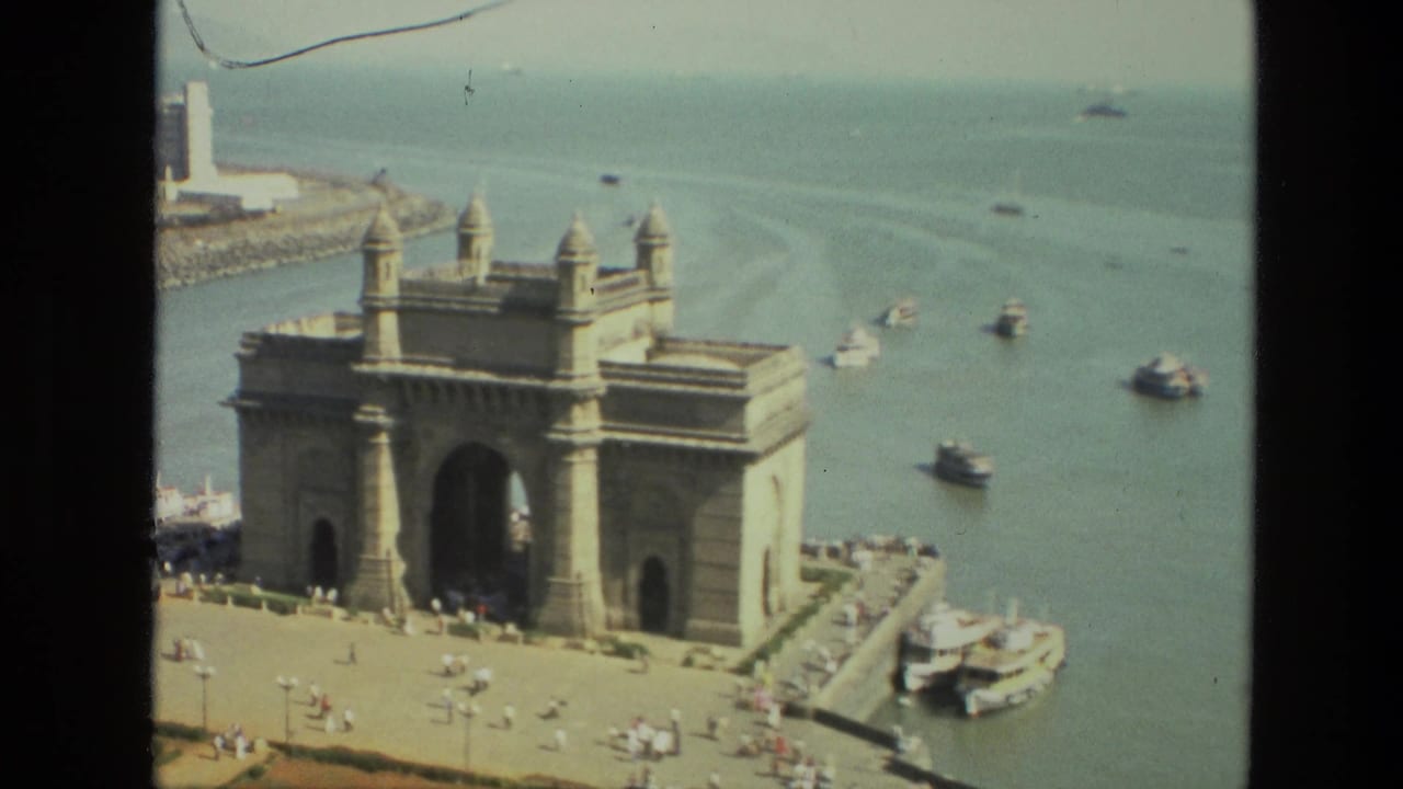Gateway of India beside harbor water with boats and visitors on the plaza.