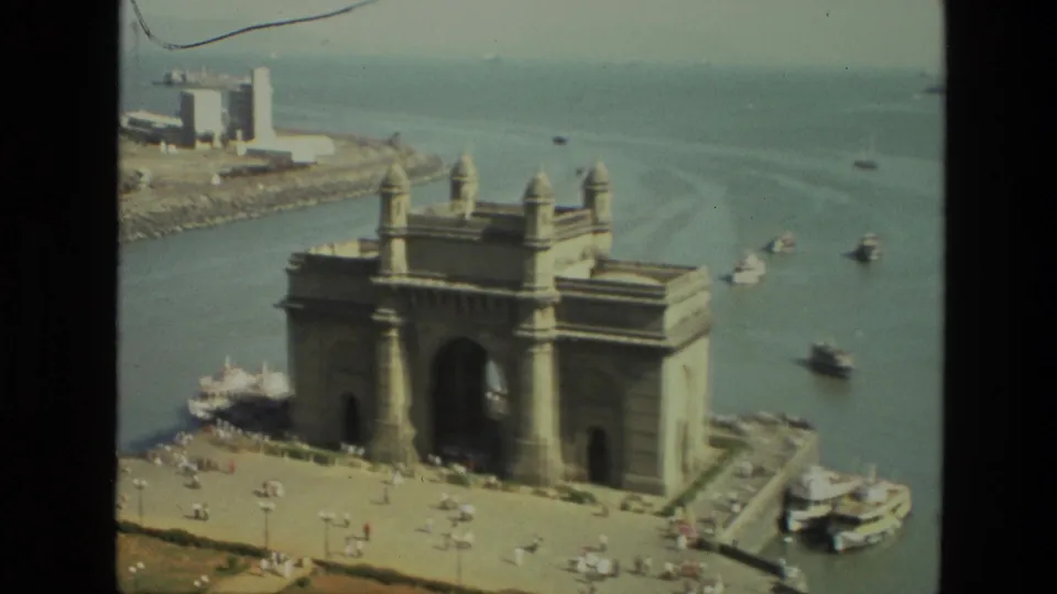 Elevated 1974 home-movie view of the Gateway of India, with boats on the water and visitors scattered across the plaza below.