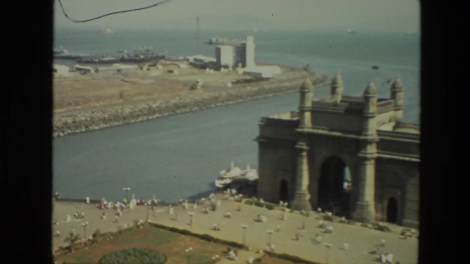 The Gateway of India appears at the right edge of this 1974 8mm frame, with the waterfront plaza, harbor water, and boats in view.