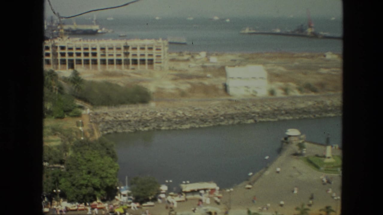 Harbor-like waterway with promenade, monument, trees, shoreline construction, and ships in the distance.
