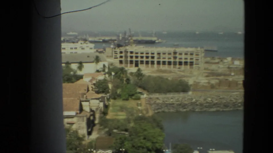 1974 India home-movie frame showing a coastal city and harbor area viewed from inside or behind a dark window frame.