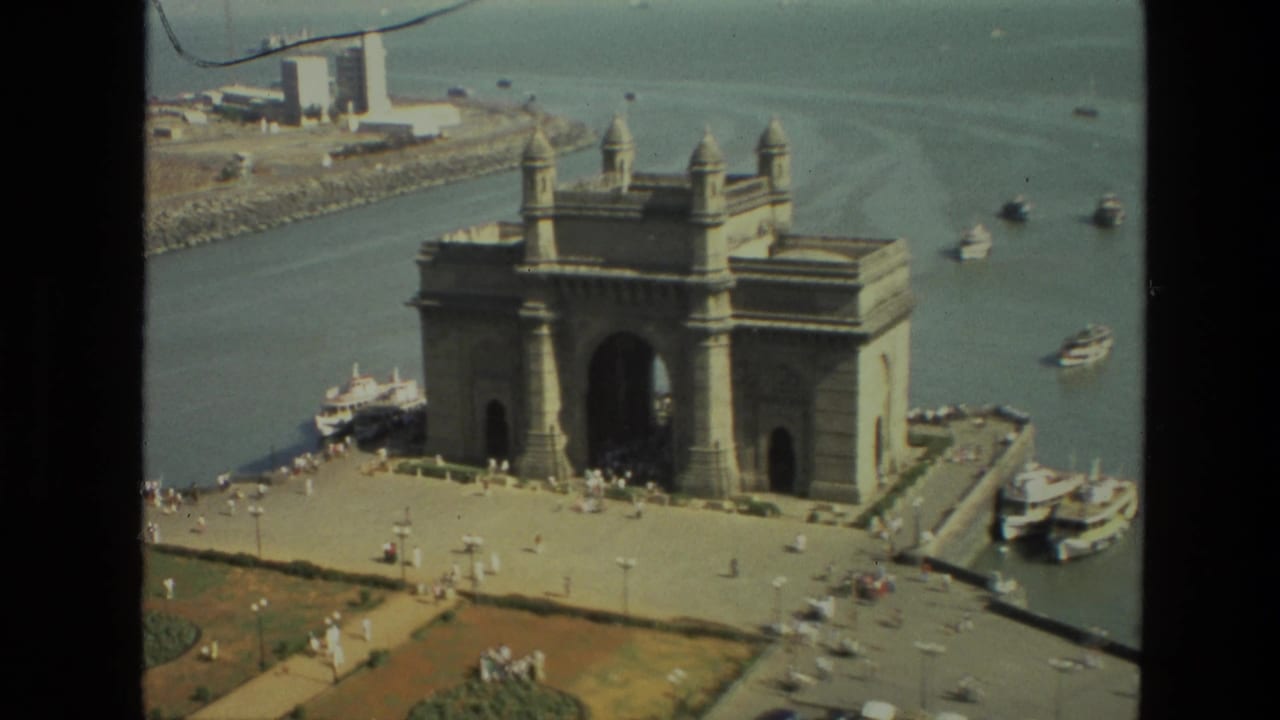 Gateway of India seen from above with plaza visitors, harbor water, and boats nearby.