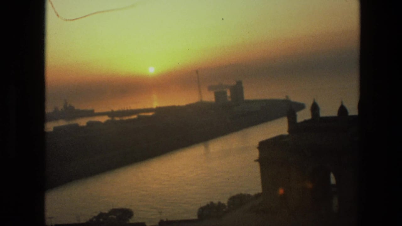 Warm 1974 India harbor view at sunset, showing reflective water, silhouetted ships, and the Gateway of India edge in shadow.
