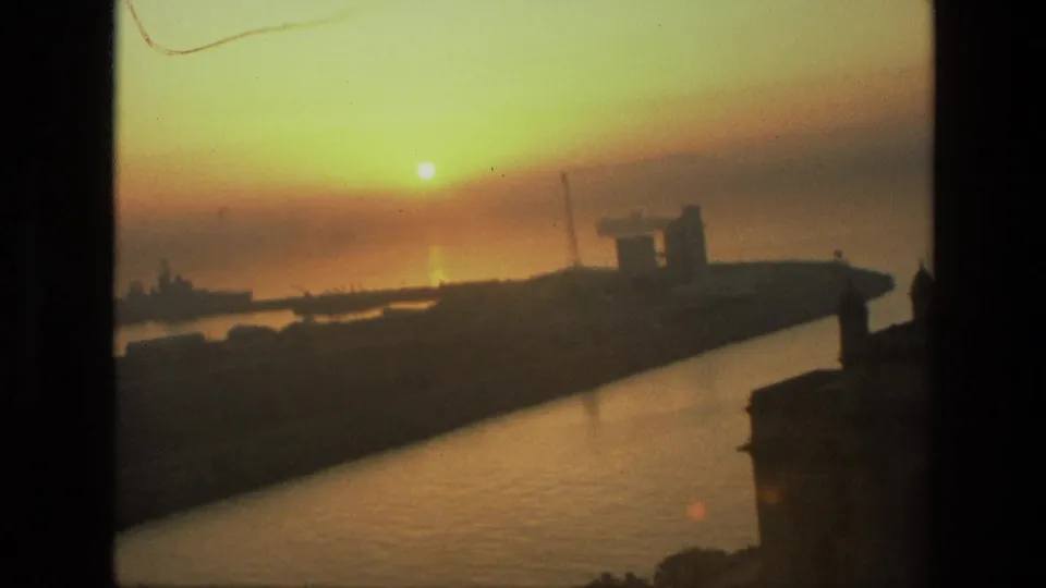 Handheld 8mm frame from India in 1974, with a tilted sunset view over harbor water and the Gateway of India in shadow.