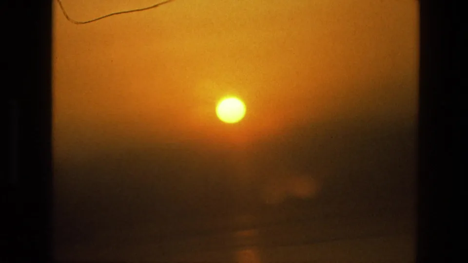 1974 India 8mm frame focused on the enlarged setting sun, with heavy haze and faint water detail below.