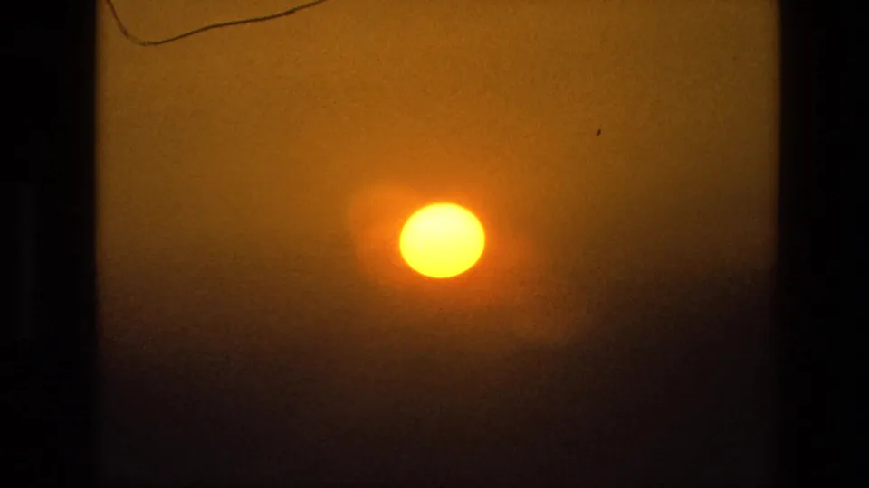 1974 India 8mm frame showing a bright sun surrounded by dense haze, with only faint bay and shoreline detail visible.
