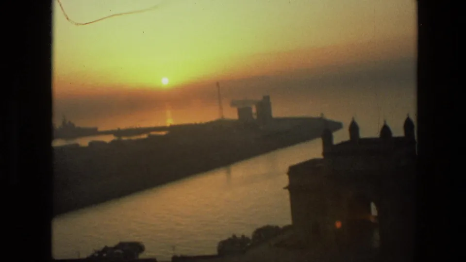 1974 India 8mm frame showing a coastal channel at sunset, with port silhouettes and a dark structure at the right edge.