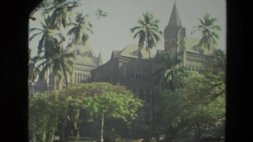 1974 India travel frame showing a large spired historic building partly obscured by palm trees and dense greenery.
