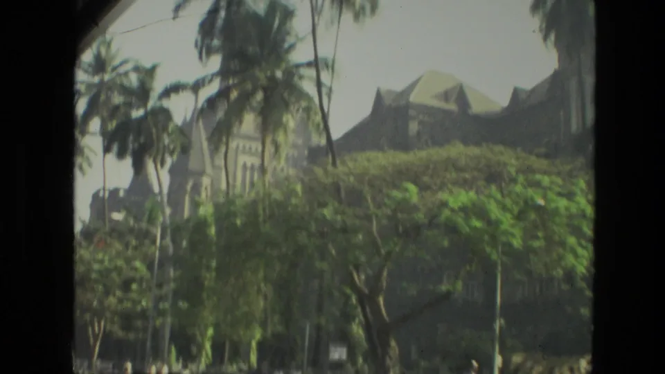 A 1974 India sightseeing view of a large building behind palms, seen through a dark window or film-frame edge.