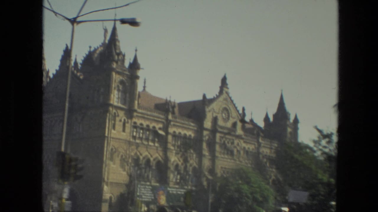 1974 8mm view of Mumbai's Chhatrapati Shivaji Maharaj Terminus facade with spires, arches, a streetlamp, and soft exposure.