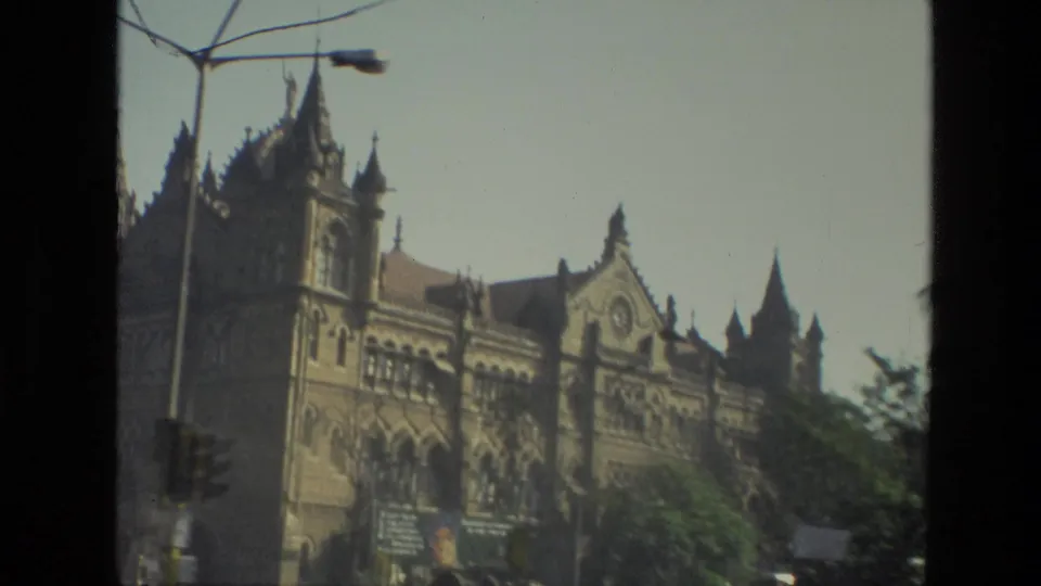 1974 8mm view of Mumbai's Chhatrapati Shivaji Maharaj Terminus facade with spires, arches, a streetlamp, and soft exposure.
