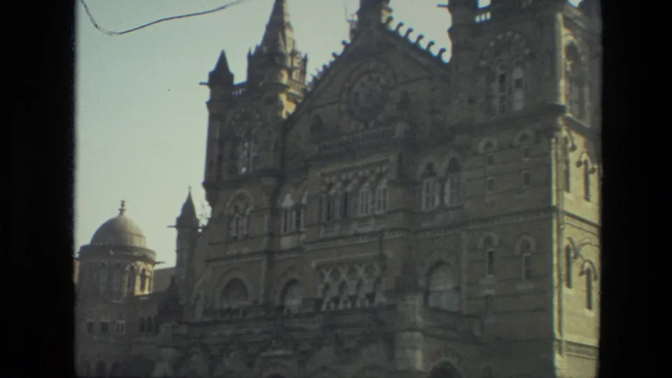 Angled 1974 8mm view of the Mumbai terminus exterior, with a dome, spired roofline, and arched stonework softened by motion.