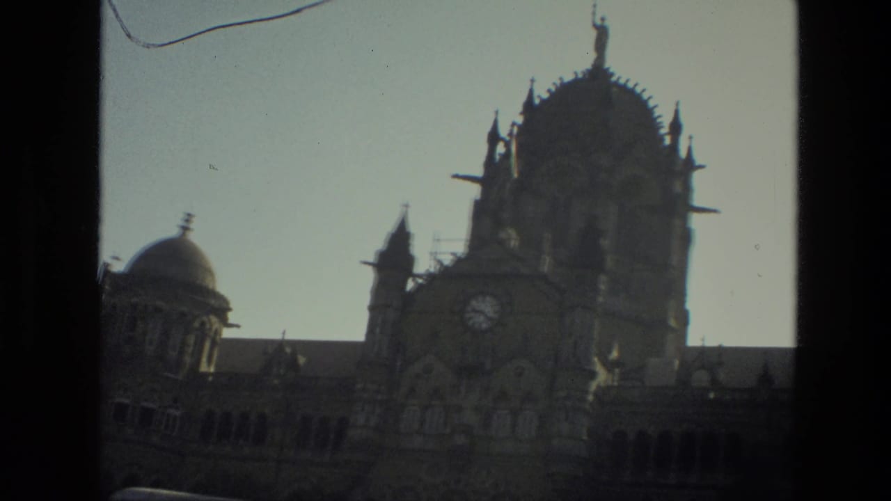 1974 India home-movie frame with a soft, handheld view of an ornate clock tower and domed historic facade.