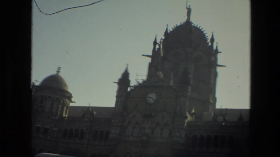 1974 India home-movie frame with a soft, handheld view of an ornate clock tower and domed historic facade.