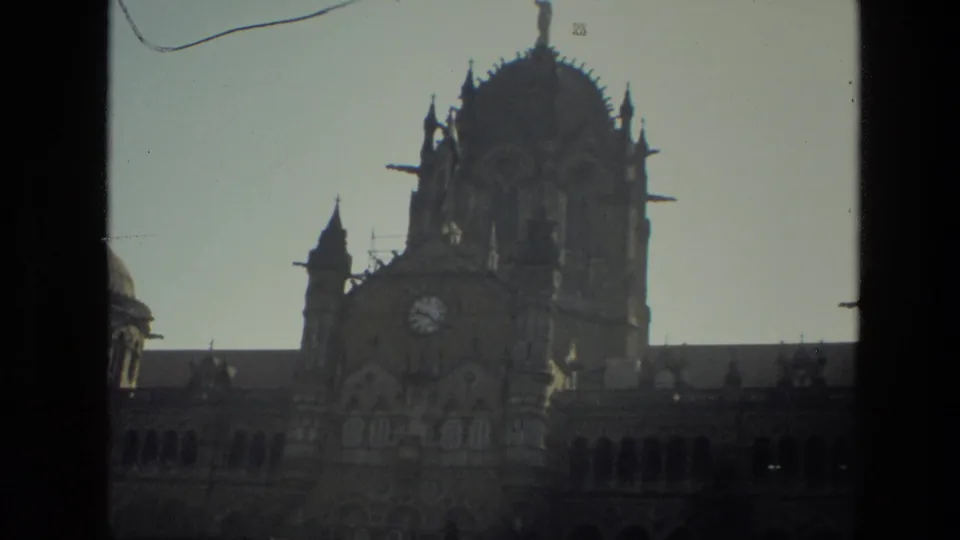 1974 India 8mm frame showing a tall ornate clock tower and arched building facade from a low street angle.