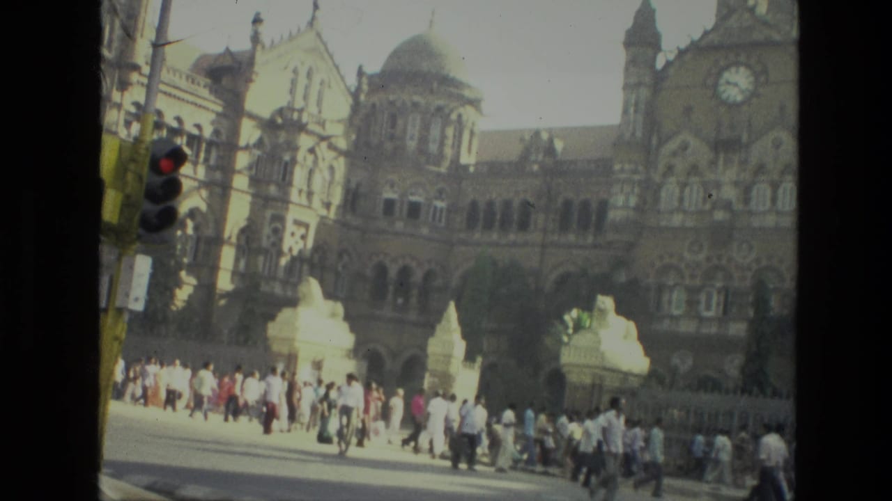 1974 India street view with many people walking past a large domed, arched building while a traffic light stands in the foreground.
