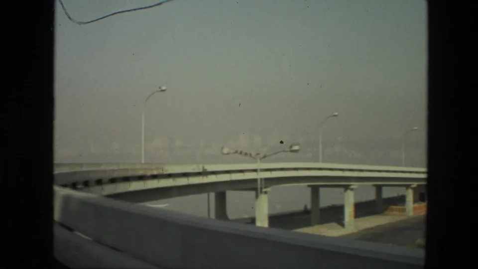 1974 India 8mm frame of concrete highway overpasses, streetlights, and a hazy skyline viewed from road level.
