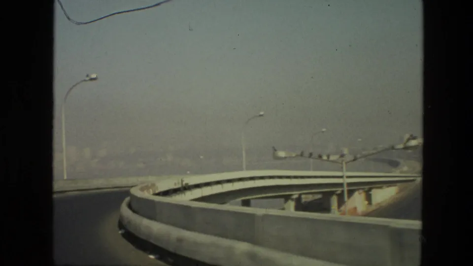 1974 India road scene showing a broad curved overpass, lamp posts, and soft atmospheric haze in an 8mm home-movie frame.
