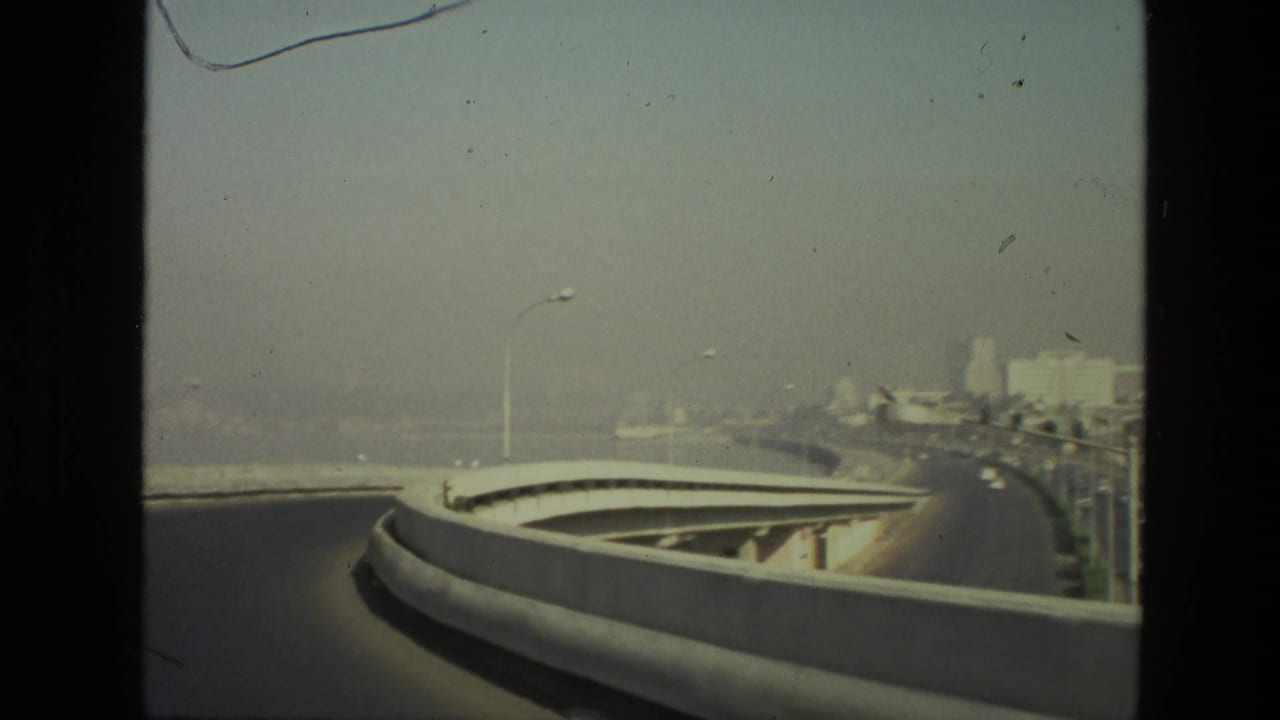 Curved elevated roadway seen from a moving vehicle under a hazy sky.