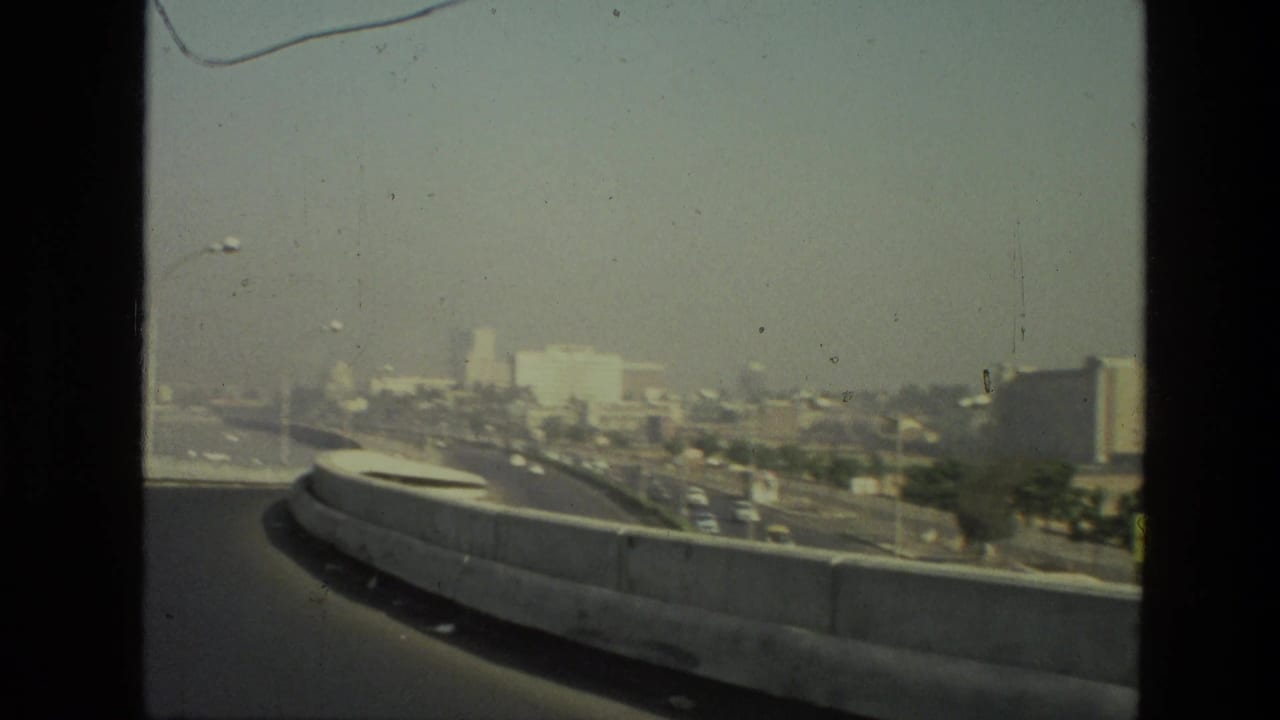 Concrete road barrier curves past a hazy urban skyline and traffic.