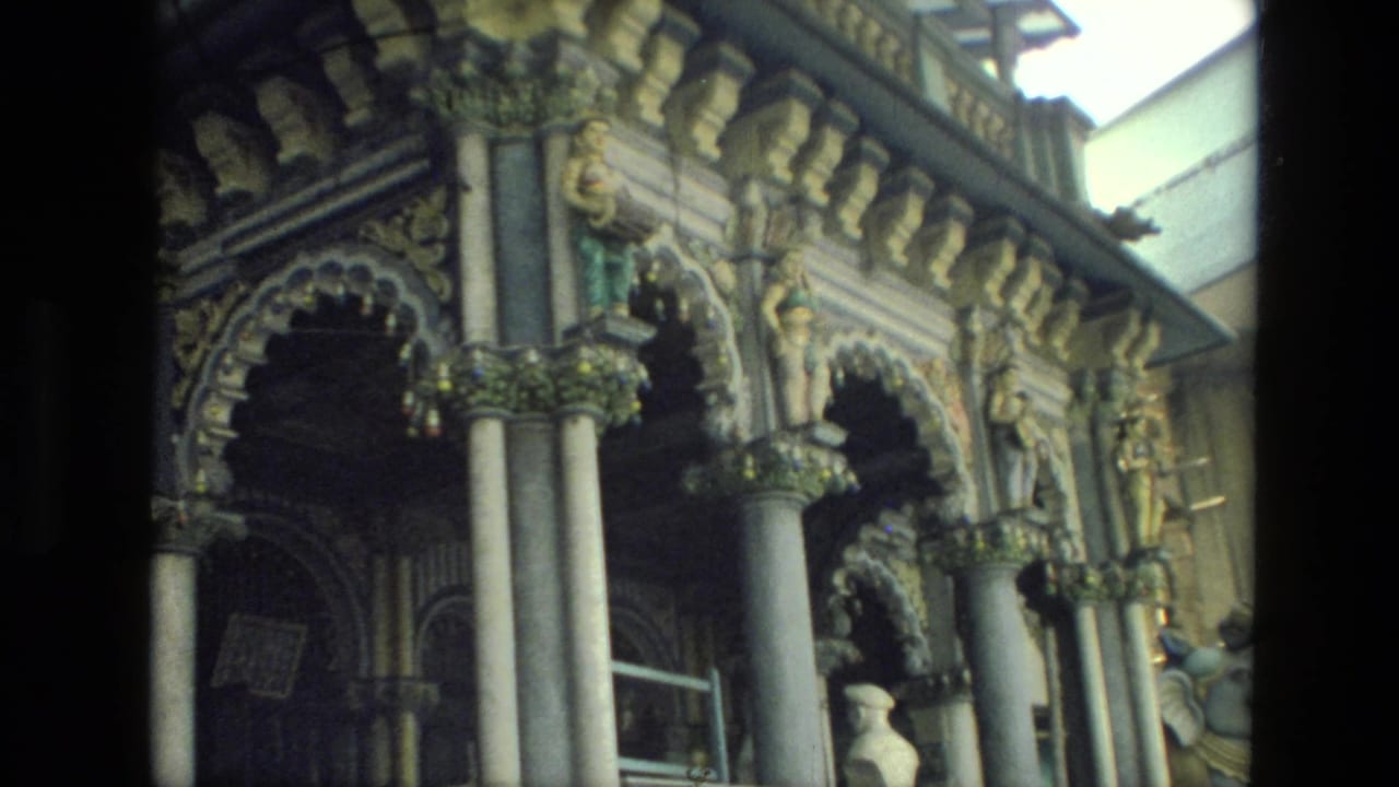 1974 India 8mm frame showing an ornate facade with arched openings, columns, carvings, and painted statuary.