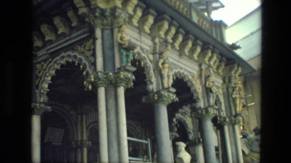 1974 India 8mm frame showing an ornate facade with arched openings, columns, carvings, and painted statuary.