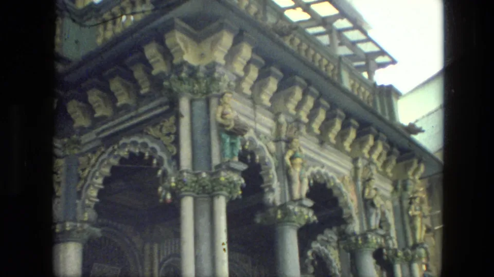 1974 India travel footage frame with a handheld view of carved arches, columns, roofline detail, and painted decorative figures.
