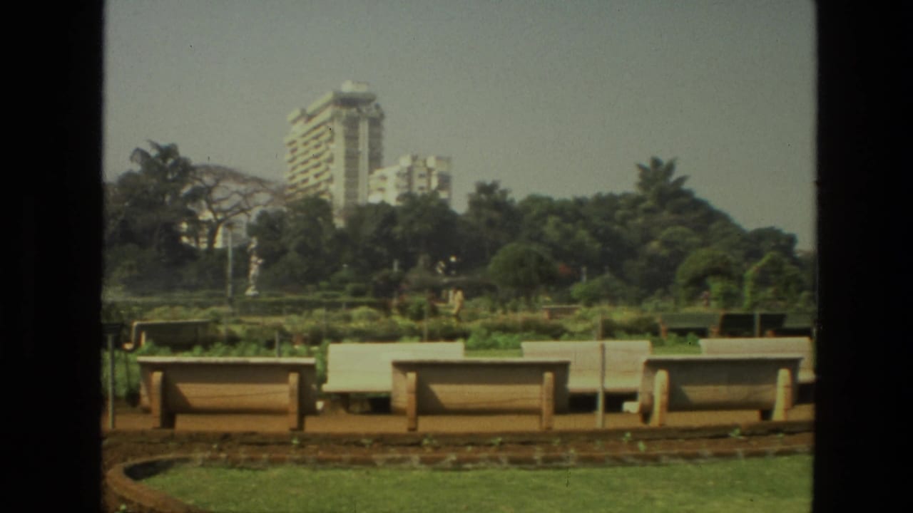 Landscaped park with benches, greenery, trees, and tall buildings beyond.