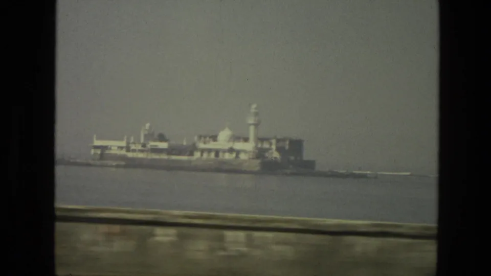 1974 India waterfront view showing a distant white island building complex across broad water from a moving vantage point.
